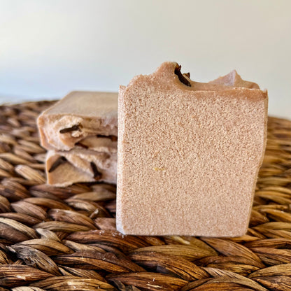 Beige sea salt soap bar with dark top piece, with smaller bars in background on mat.