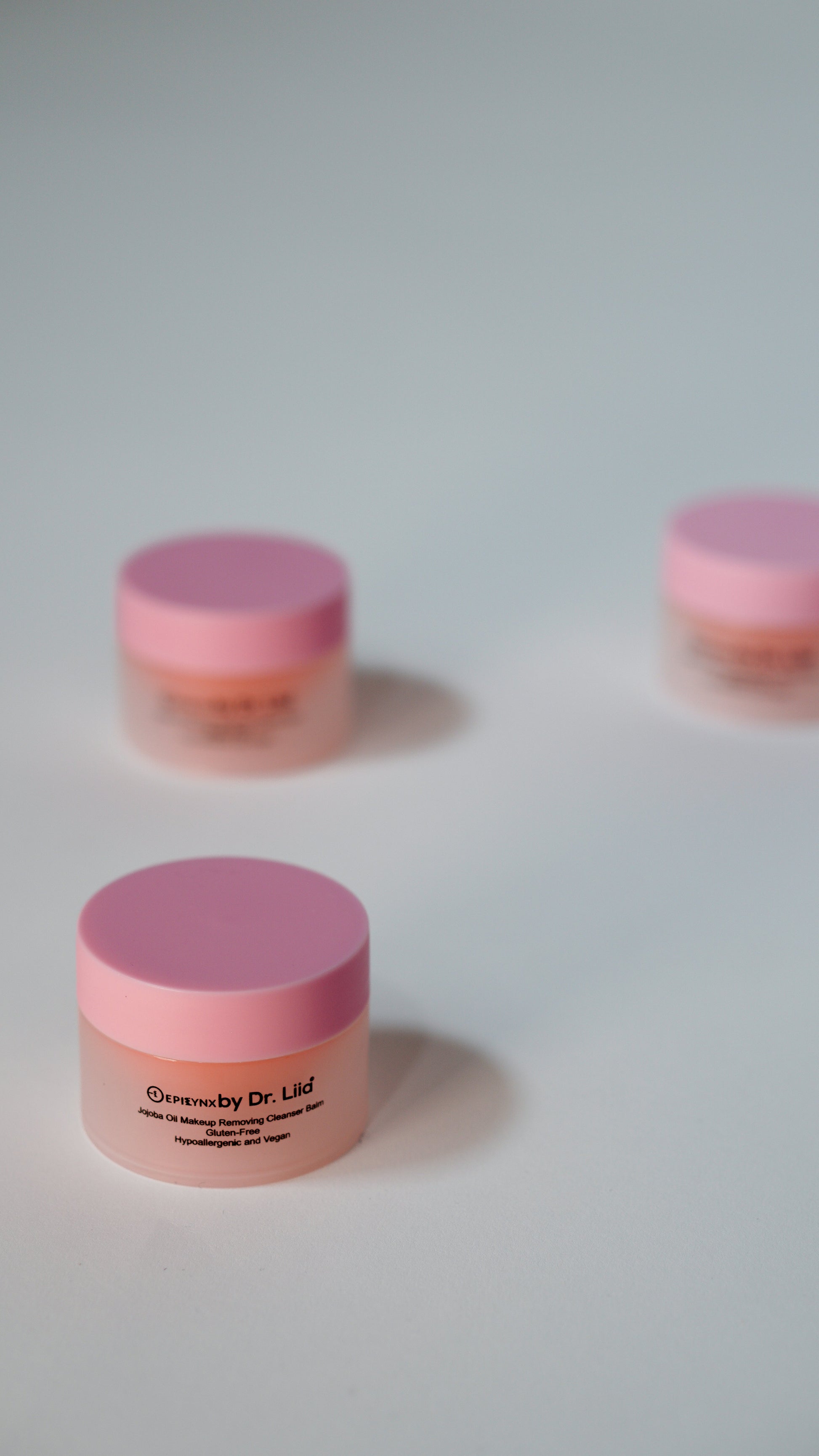 Mini jars of peach makeup remover balm with purple-pink lids