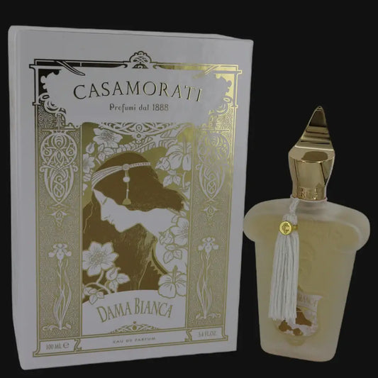Cream perfume bottle with gold cap and tassel, beside ornate gold-trim box
