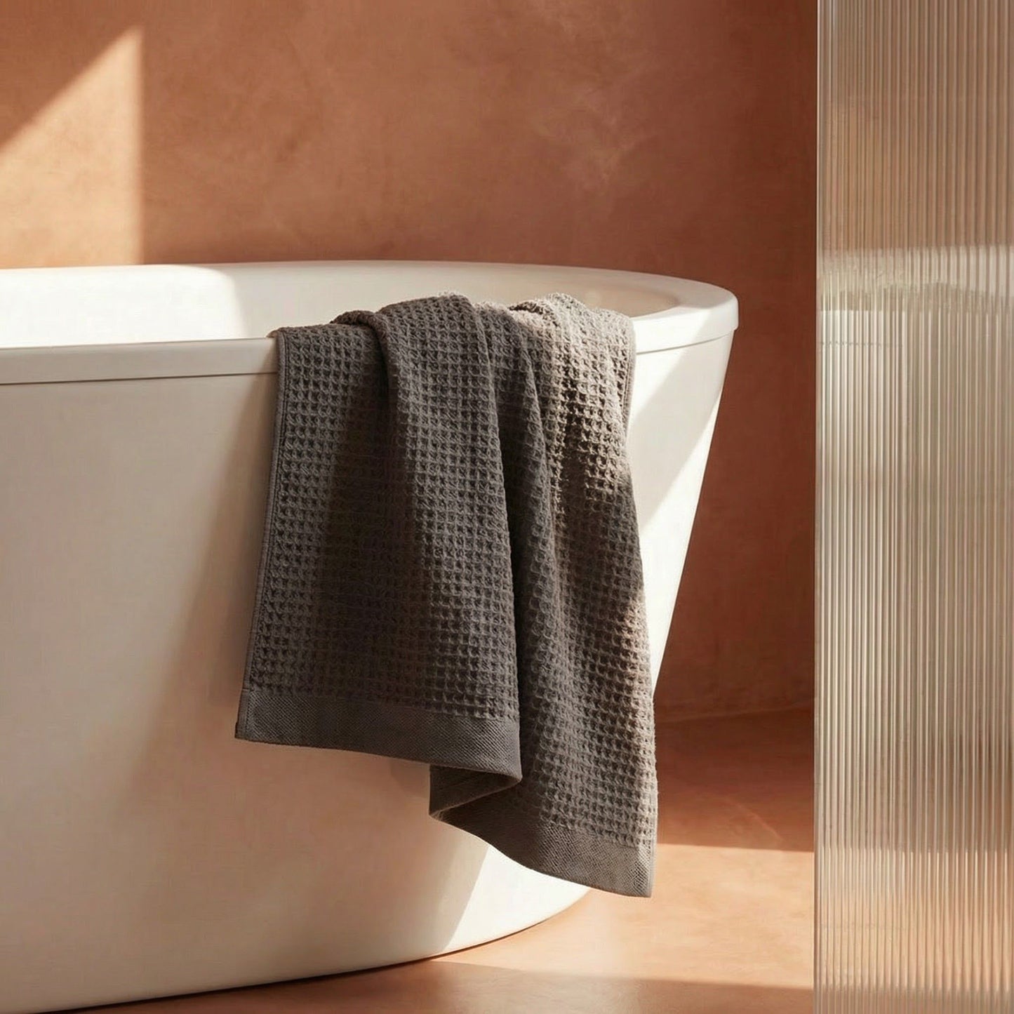 Charcoal waffle cotton towel draped over bathtub edge, textured grid weave