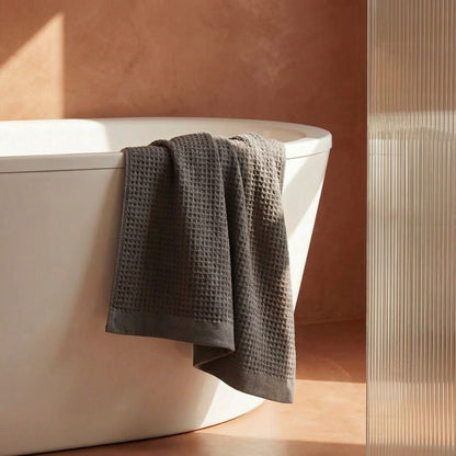 Charcoal waffle cotton towel draped over bathtub edge, textured grid weave