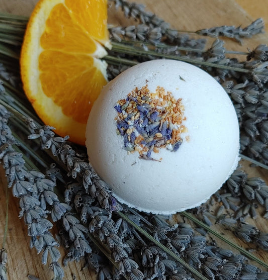 White bath bomb with blue flower bits, surrounded by lavender and an orange slice