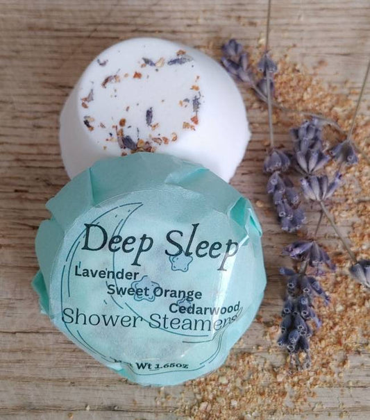 Shower steamer disc with white base, dried lavender bits, and aqua label wrap