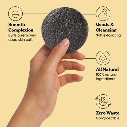 Charcoal facial cleansing sponge held in hand, round dark gray exfoliating pad