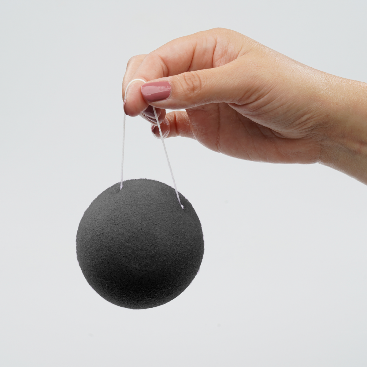 Round charcoal konjac cleansing sponge with hanging loop, held by hand