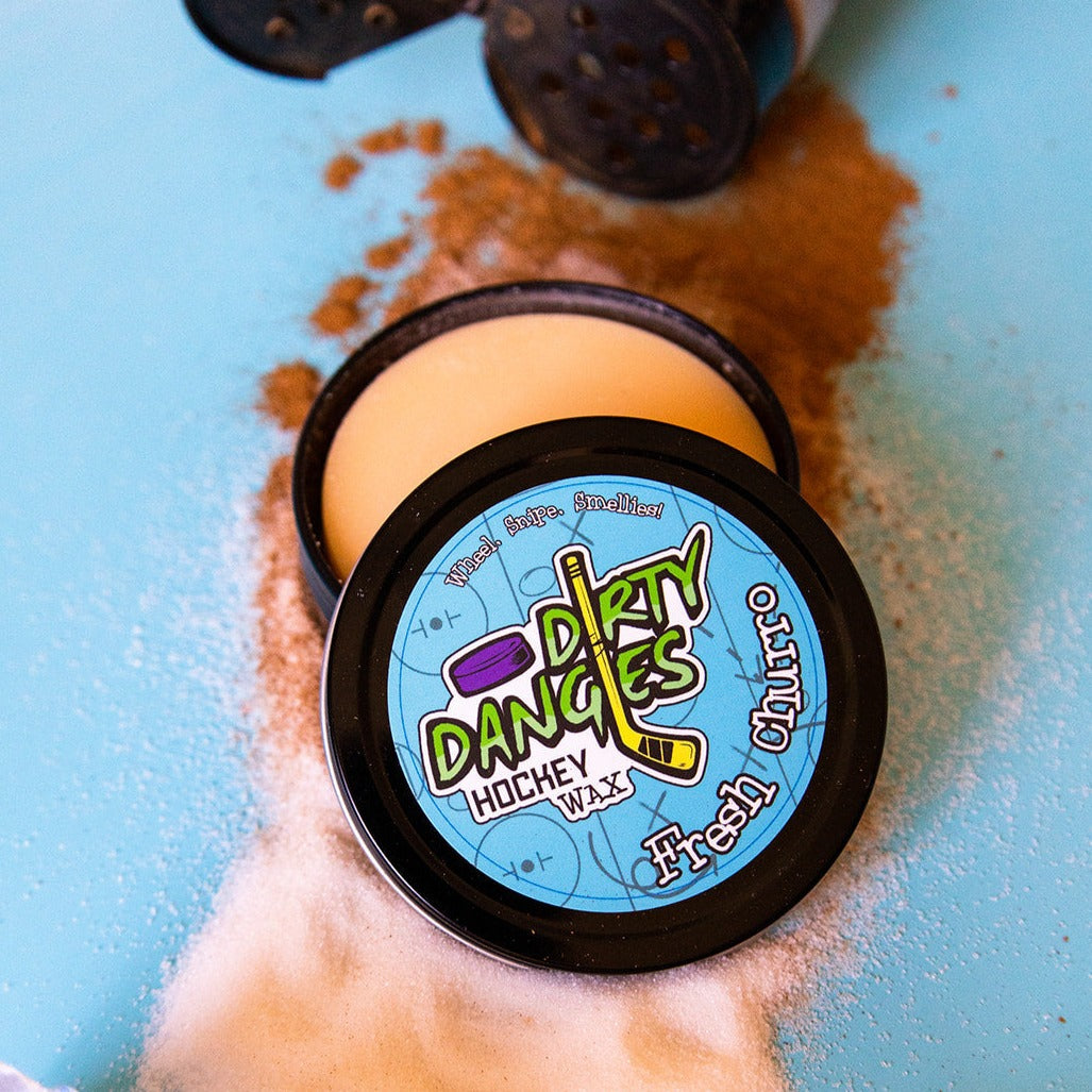 Round hockey wax tin with peach-colored wax and black lid with Dirty Dangles logo