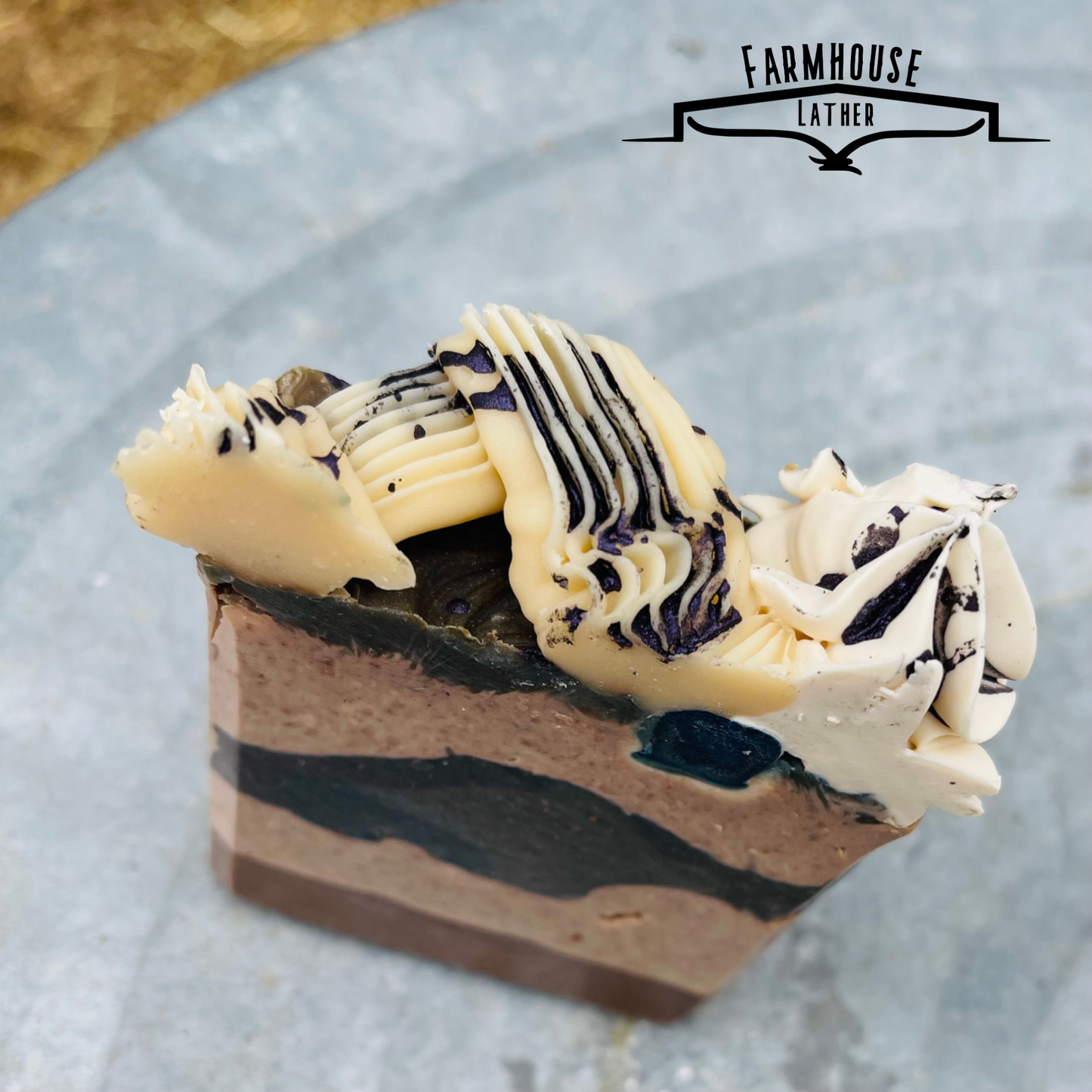 Handmade soap bar with black-blue stripe layers and white swirl topping