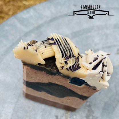 Handmade soap bar with black-blue stripe layers and white swirl topping