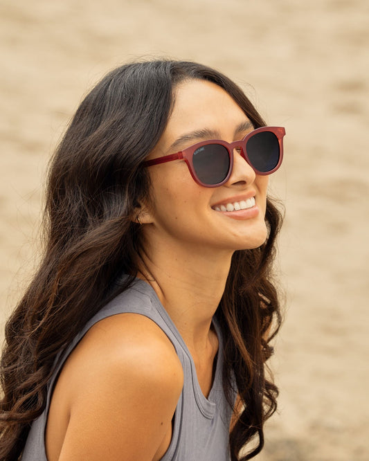 Polarized sunglasses on a person, maroon frames with dark lenses