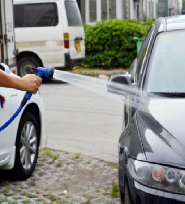 Blue flexible hose spraying water toward a parked car