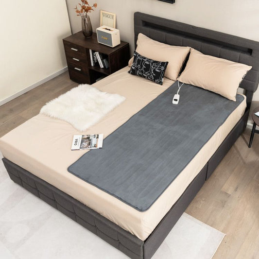 Gray heated mattress pad laid on bed with remote controller and attached power cord.