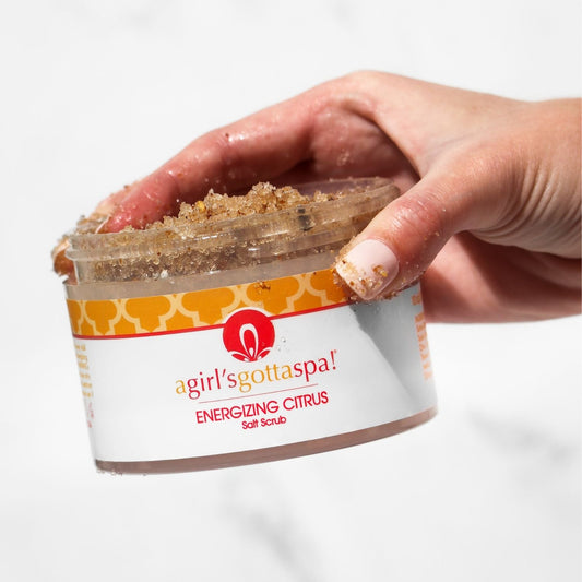 Body scrub jar opened with hands scooping brown salt scrub