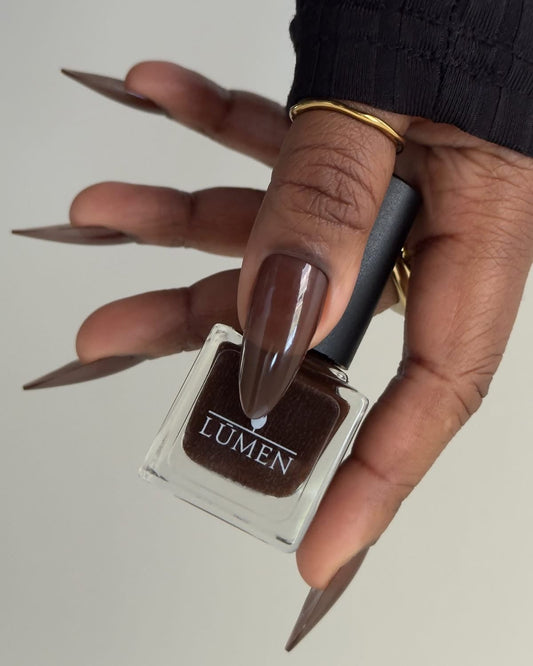 LUMEN nail polish bottle with glossy espresso-brown finish on long pointed nails.