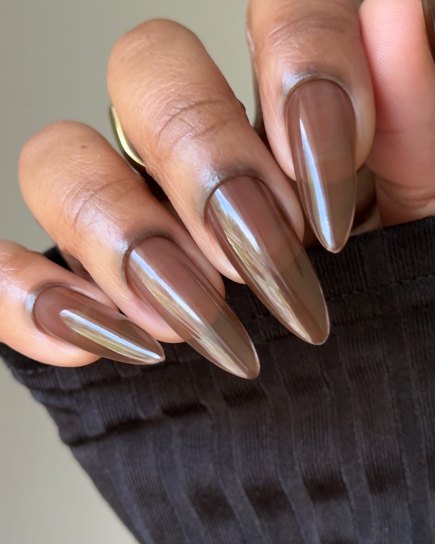 Long almond nails with glossy espresso-brown polish, close-up on hand.