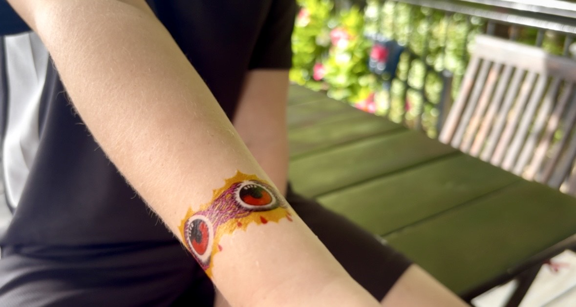 Temporary tattoo band on wrist with red eyeball faces and purple swirls