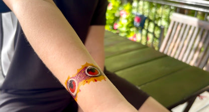 Temporary tattoo band on wrist with red eyeball faces and purple swirls