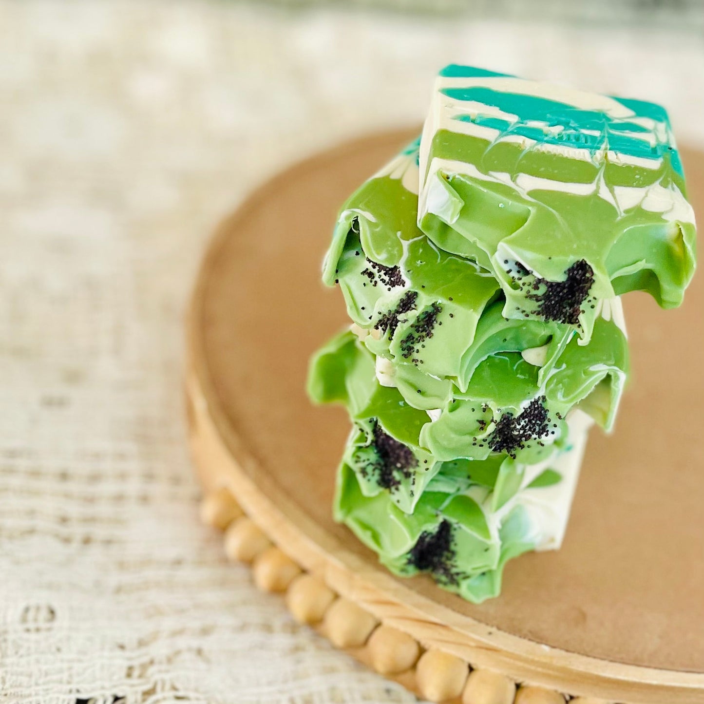 Close-up of layered green soap bar with teal top and black speckles on a wooden board.