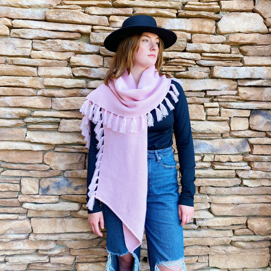 Pink knit blanket scarf with long tassel fringe, draped around a model’s neck