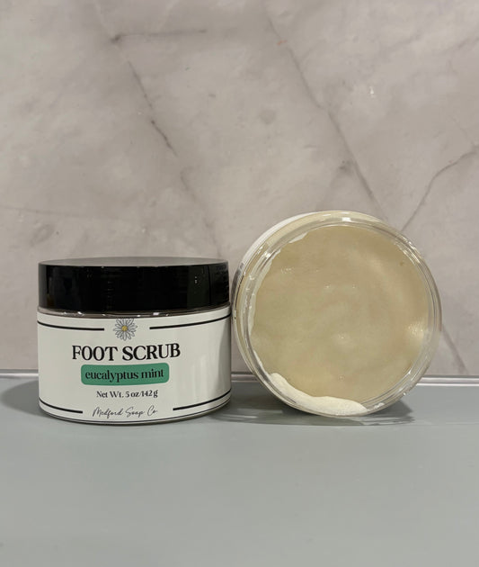 Foot scrub jar with black lid; eucalyptus mint label; cream scrub in open container.