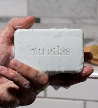 Exfoliating bar soap in hand, pale cream with blue specks, damp and lathered