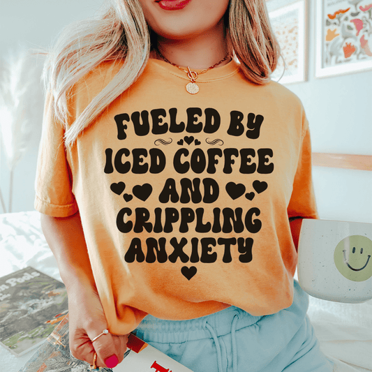 Peach T-shirt with bold 'FUELED BY ICED COFFEE AND CRIPPLING ANXIETY' graphic