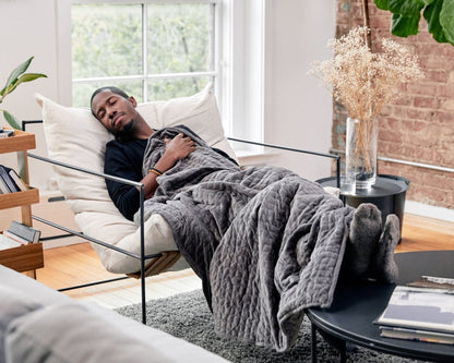 Dark grey quilted weighted blanket draped over a sofa while a person rests