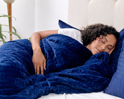 Blue weighted blanket tucked around a sleeper on a bed