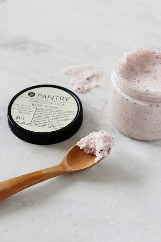 Exfoliating body polish container with pink scrub and wooden spoon with some scooped