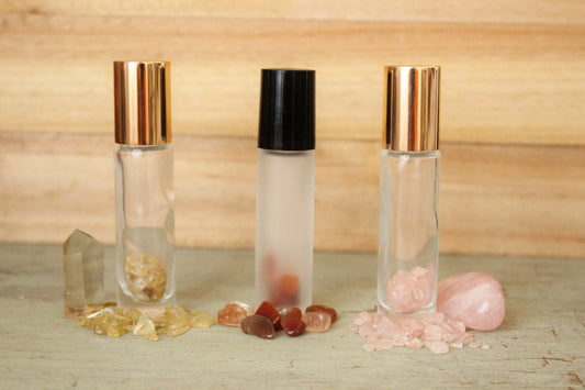 Clear frosted gemstone roller bottles with gold and black lids, surrounded by pink and yellow stones