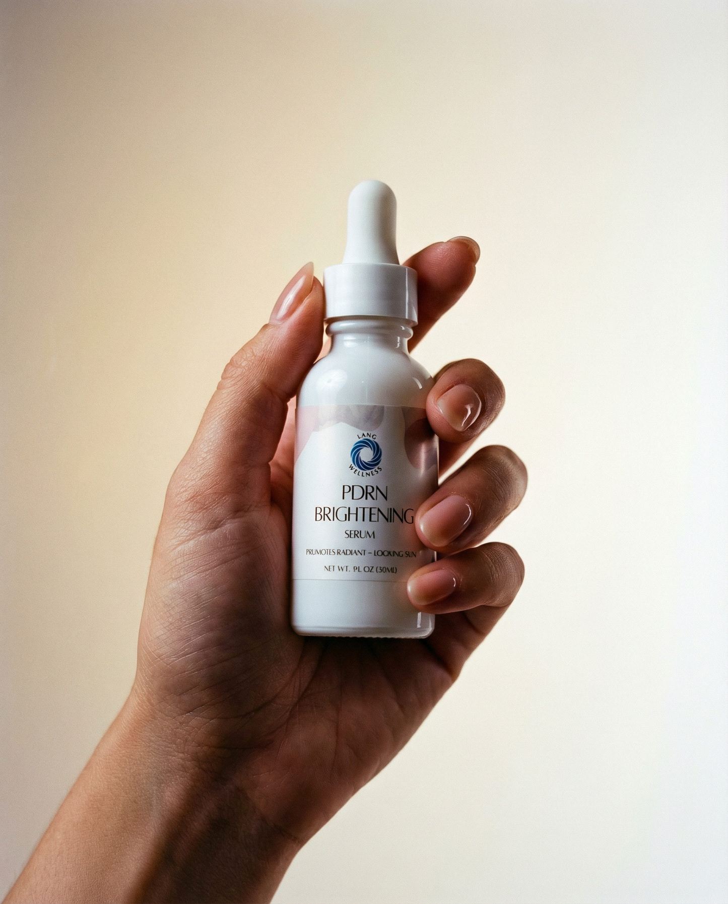 Brightening serum bottle held in hand; white dropper and label on clear glass