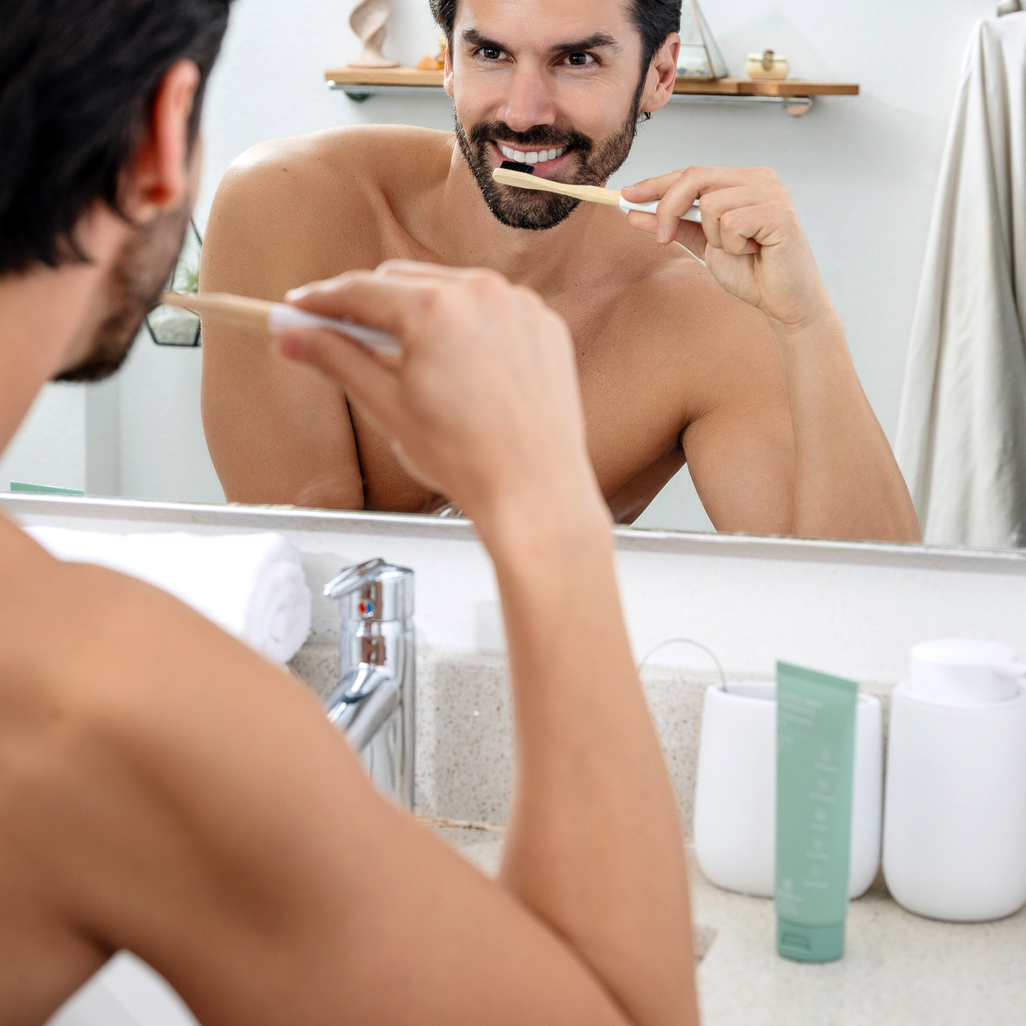 Man brushing teeth with a toothbrush while looking in a bathroom mirror