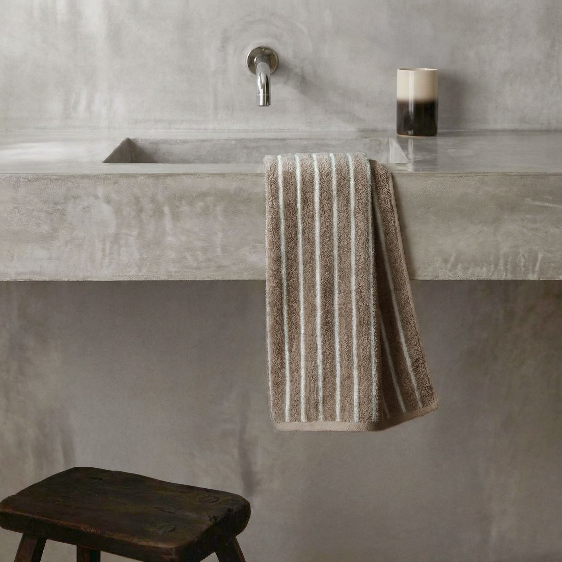 Striped towel hanging on bathroom bar, beige and white plush cotton loops