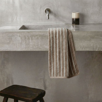 Striped towel hanging on bathroom bar, beige and white plush cotton loops