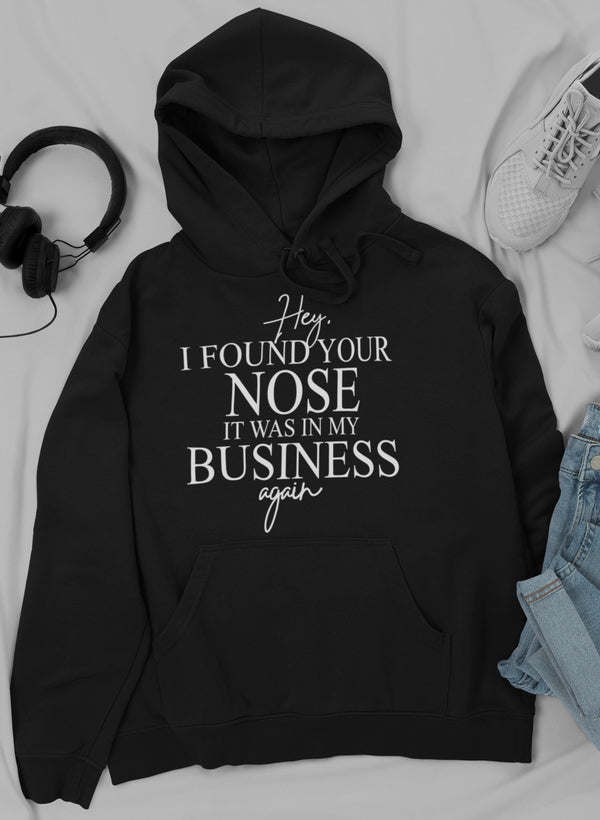 Black hoodie with front pocket, drawstring hood, and “I FOUND YOUR NOSE” quote print