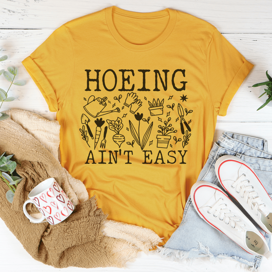 Gold T-shirt with "HOEING AIN'T EASY" floral tool graphic on chest