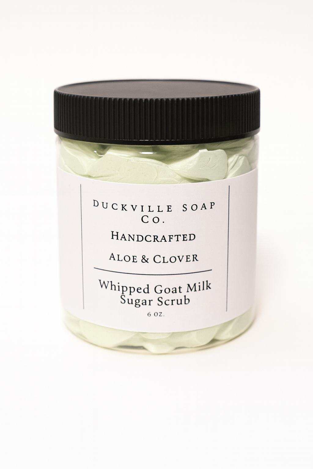 Whipped goat milk sugar scrub jar, Aloe & Clover label, black lid, light green flakes