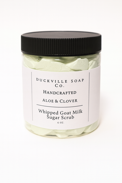 Whipped goat milk sugar scrub jar, Aloe & Clover label, black lid, light green flakes