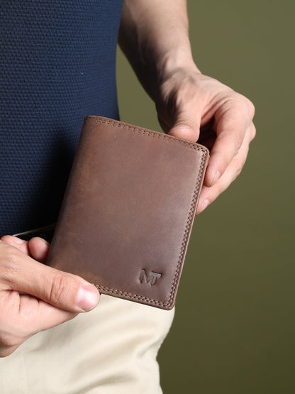 Men's brown leather wallet held in hand, showing stitched edges and MT logo.