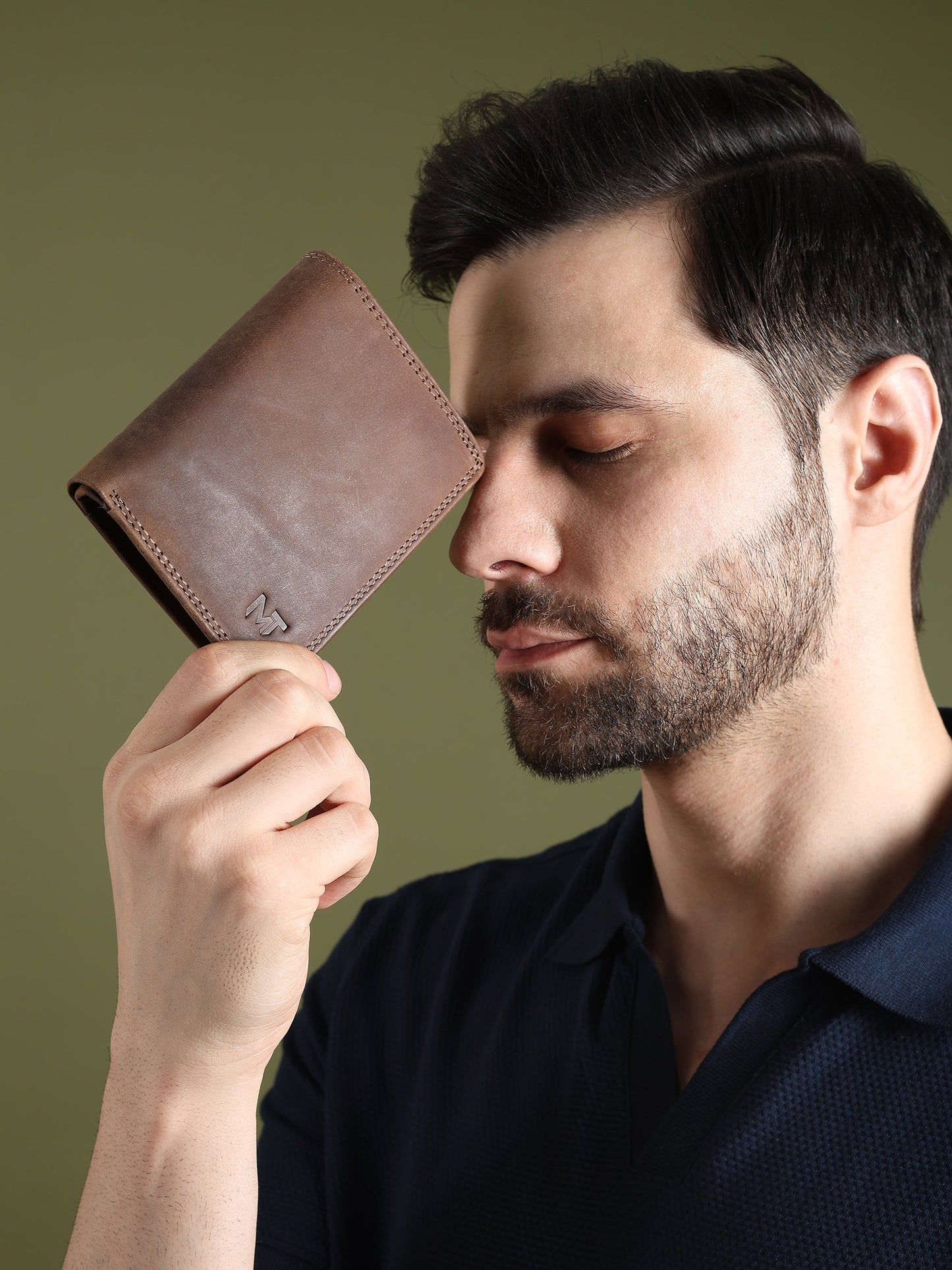Men's brown leather wallet held up by a man, showing stitched front and MT logo.