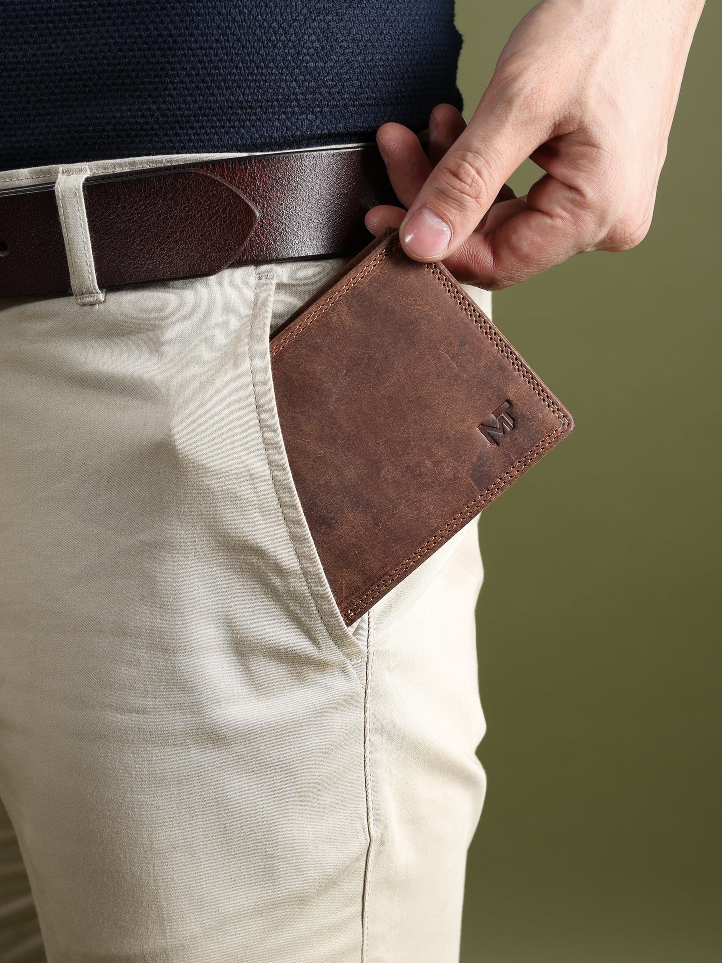 Brown leather wallet in hand with front flap and MT logo near the lower corner