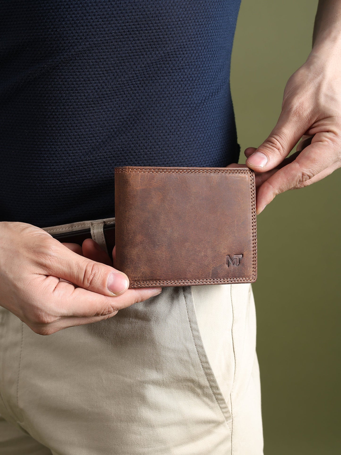 Brown leather wallet held in hands, showing stitched perimeter and MT logo patch