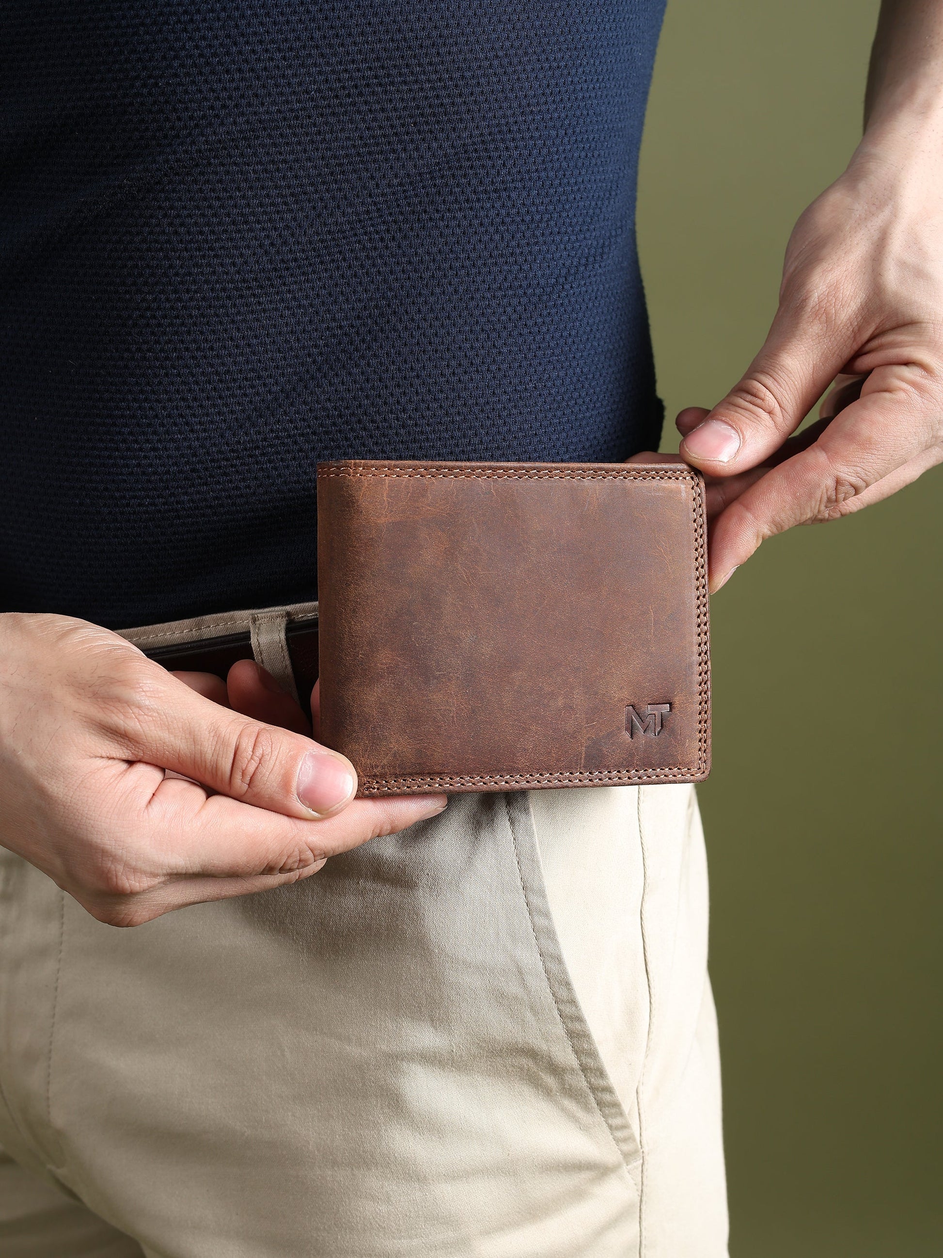 Brown leather wallet held in hands, showing stitched perimeter and MT logo patch