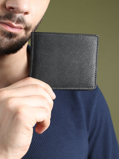 Black textured leather men’s wallet held near chest, compact bi-fold