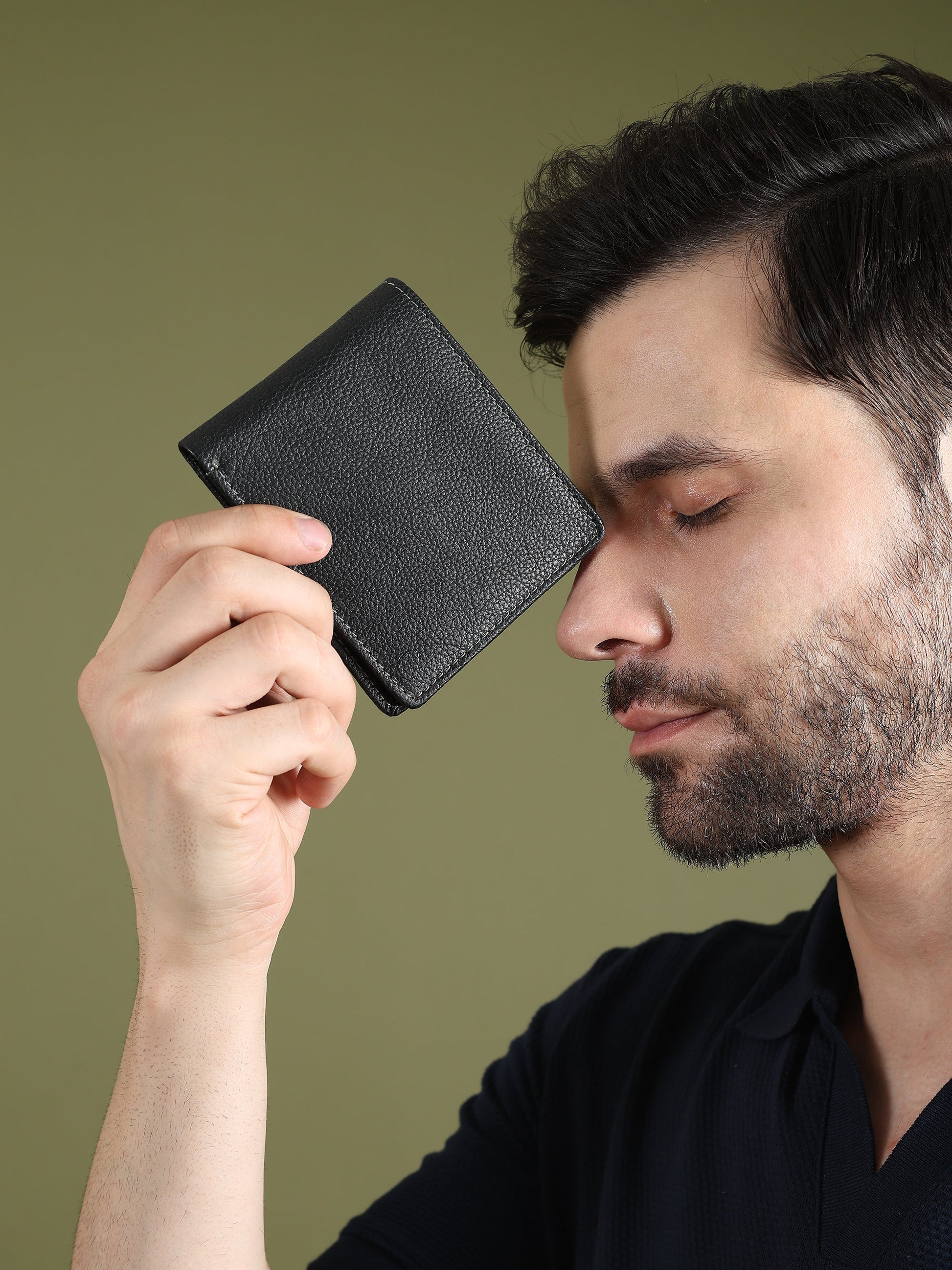 Black textured leather men’s wallet held to ear, compact square face