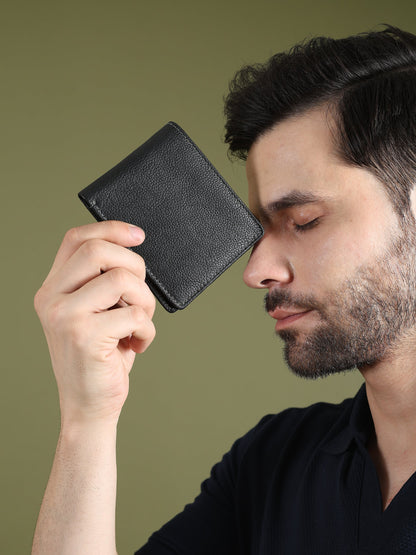Black textured leather men’s wallet held to ear, compact square face