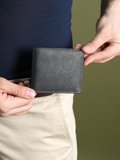 Black textured leather men’s wallet held with fingers, compact bi-fold