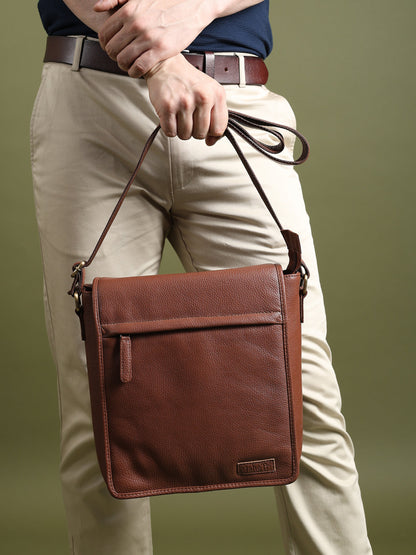 Brown leather crossbody bag worn on a person, top flap and secure side hardware