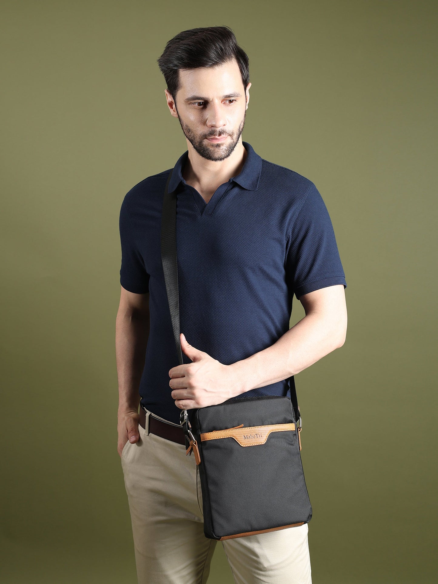 Black canvas side messenger bag with tan accents worn across the body with a shoulder strap