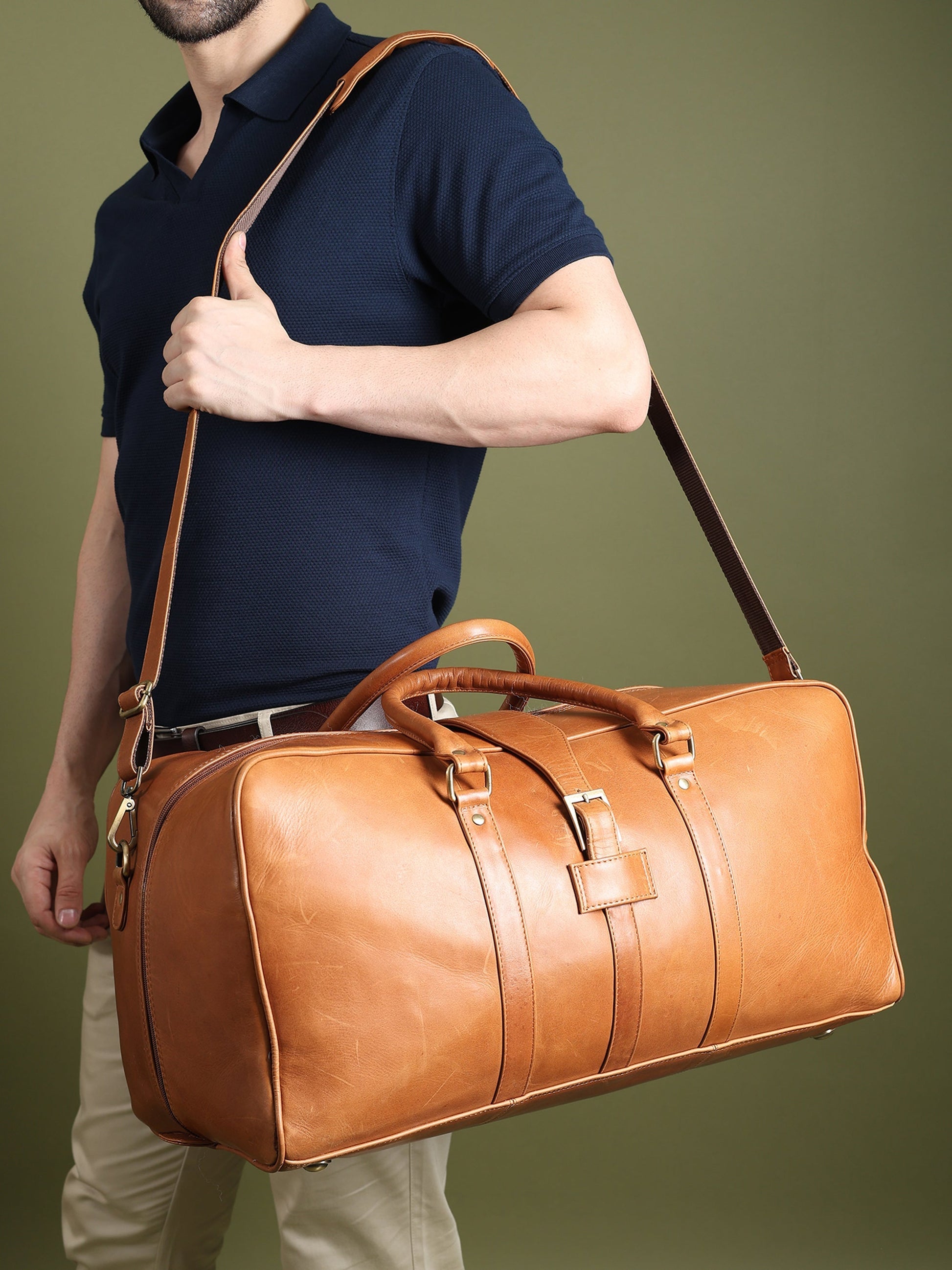 Tan leather duffle bag with crossbody strap, carried by a model