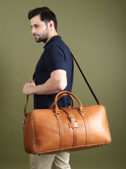 Tan leather duffle bag with long shoulder strap, carried at the side by a model